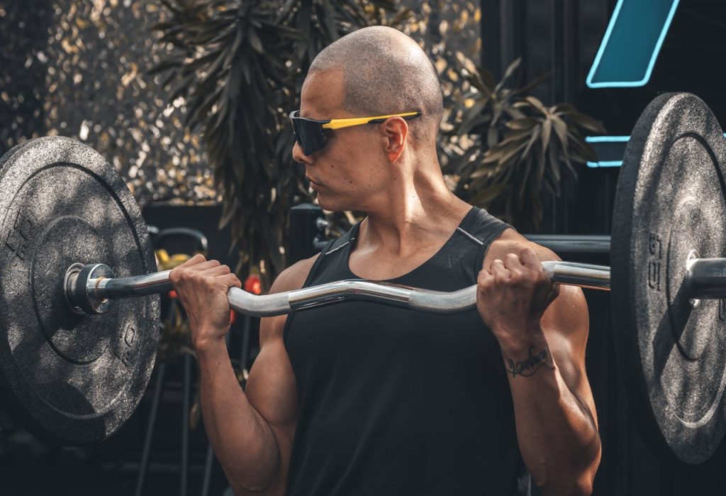 A muscular man lifts a barbell in an outdoor gym setting, showcasing strength and fitness.